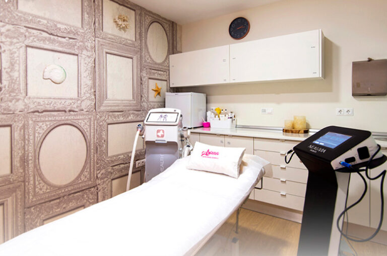 Sala para tratamiento estético en Clínica Aroma cn paredes en empapeladas en tonos grises, camilla y máquinas